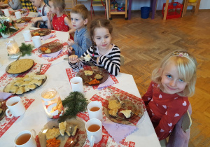 Dzieci siedzą przy świątecznym, wigilijnym stole. Kosztują tradycyjne potrawy przygotowane przez nasze Panie Kucharki.
